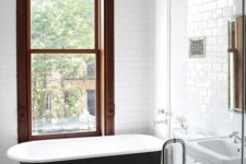 a laconic bathroom with a vintage feel, a large stained frame double-hung window, a black free-standing tub and a glass-enclosed shower