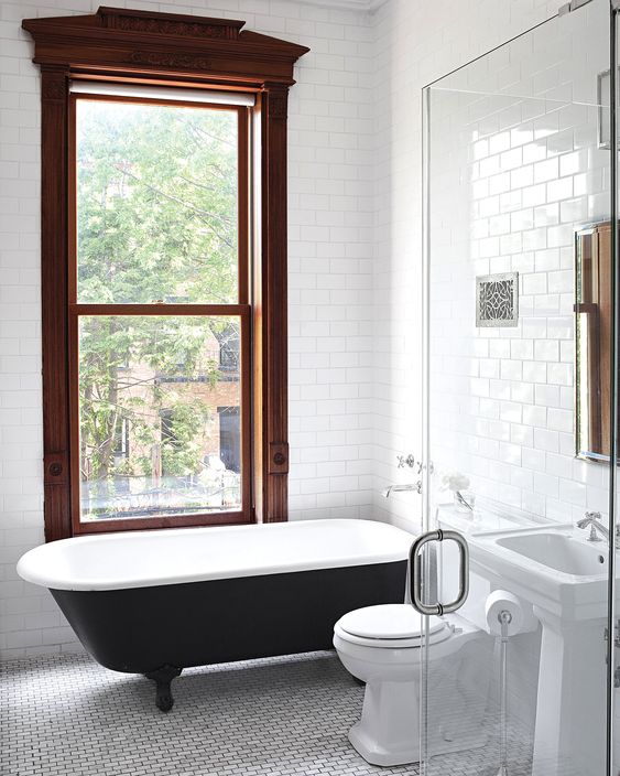 a laconic bathroom with a vintage feel, a large stained frame double-hung window, a black free-standing tub and a glass-enclosed shower