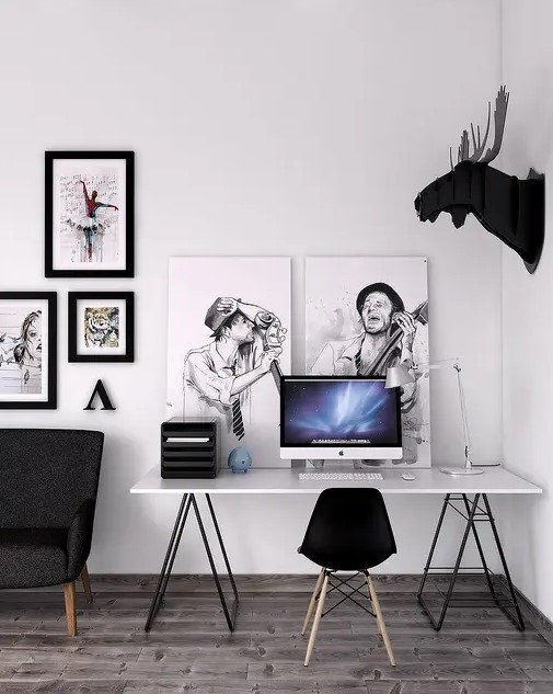 a laconic black and white Scandinavian home office nook with a trestle desk, a black Eames chair, black and white artworks, faux taxidermy and other stuff