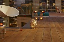 a large balcony clad with coppered oak, with modern furniture, teal Moroccan poufs and candle lanterns all around