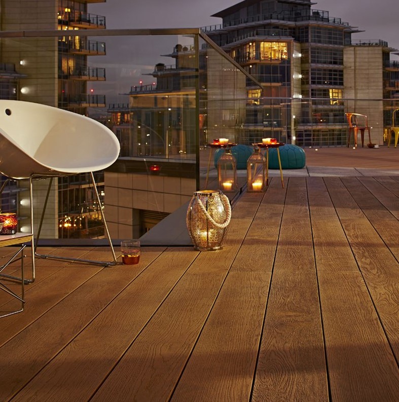 a large balcony clad with coppered oak, with modern furniture, teal Moroccan poufs and candle lanterns all around