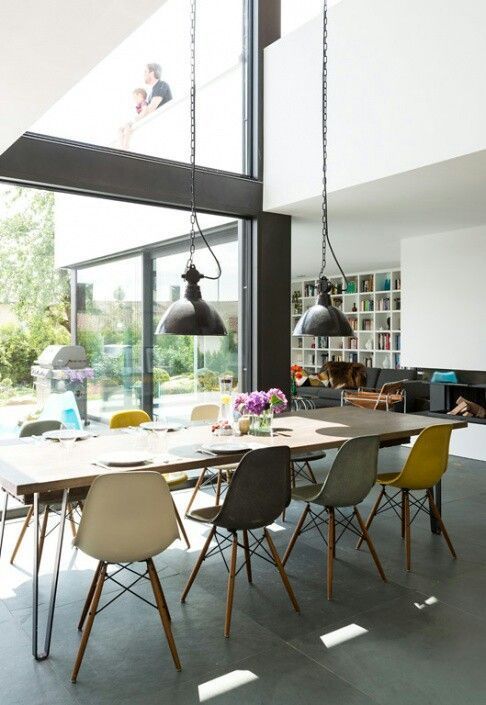 a light-filled dining space with a long dining table, colorful Eames chairs, black pendant lamps over the table