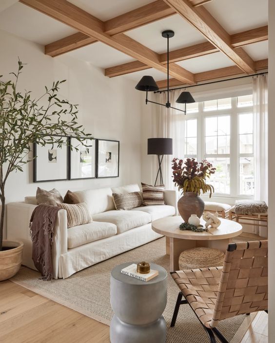 a light-filled earthy living room with wooden beams, a white sofa, stools and a woven chair, a grey side table and a round coffee table