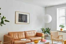 a light-filled mid-century modern living room with an amber leather sofa, neutral chairs and a simple coffee table, a pendant lamp