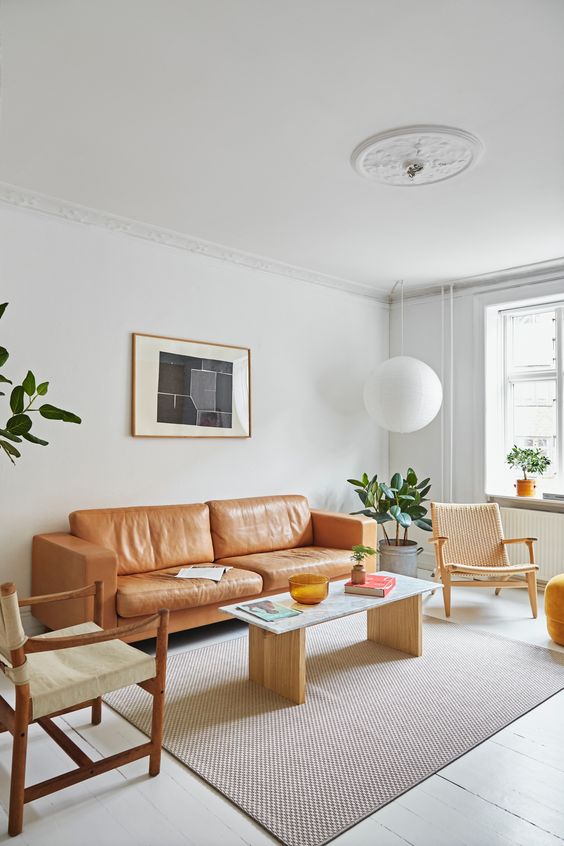 a light-filled mid-century modern living room with an amber leather sofa, neutral chairs and a simple coffee table, a pendant lamp