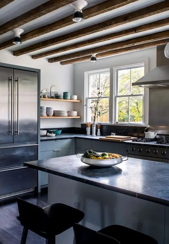a light grey kitchen with flat panel cabinets and a kitchen island, black soapstone countertops and a backsplash, wooden beams and open shelves
