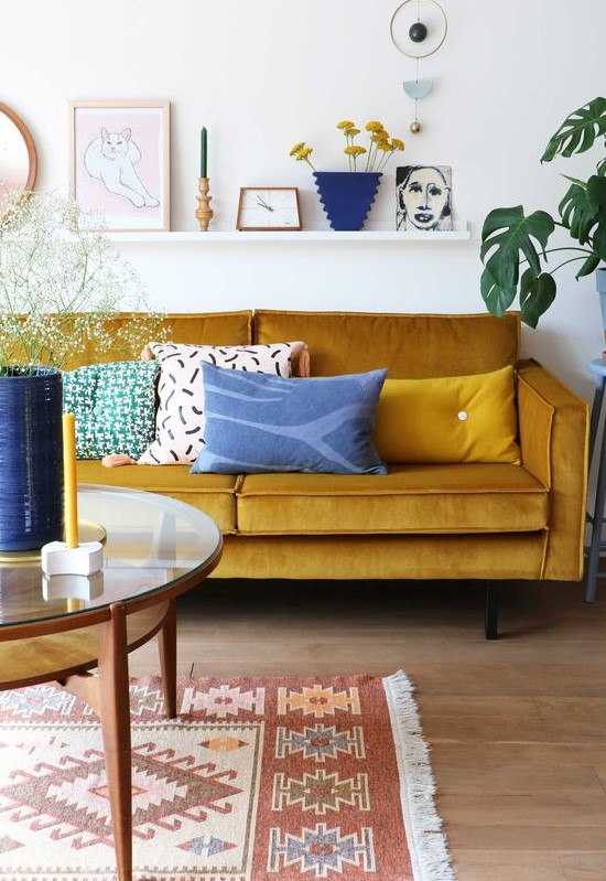 a lively living room with a mustard sofa, a round table, a ledge gallery wall and touches of blue for a contrast