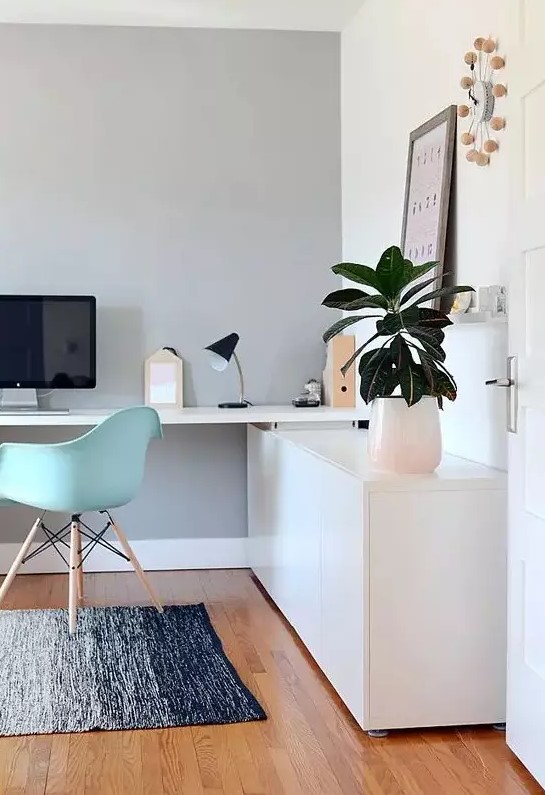 a lovely Scandinavian home office with a sleek storage unit and a built-in desk, a mint blue Eames chair, potted greenery and a cool clock