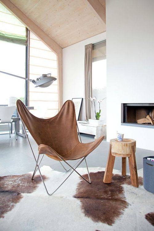 a lovely and airy nook by the fireplace, with a brown leather butterfly chair, a wooden stool and a basket with magazines