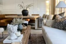 a lovely earthy open layout with neutral seating furniture, a low rough coffee table, a dining zone with a rust sofa and an oval table