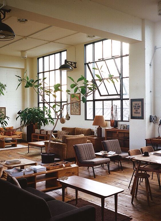 a lovely earthy tone open layout with rust and mustard furniture, grey chairs, stained tables and console tables and potted plants