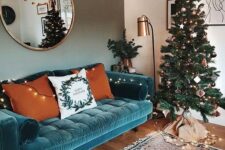 a lovely living room with a turquoise velvet sofa, a Christmas tree with lights, a floor lamp and a round mirror plus a printed rug
