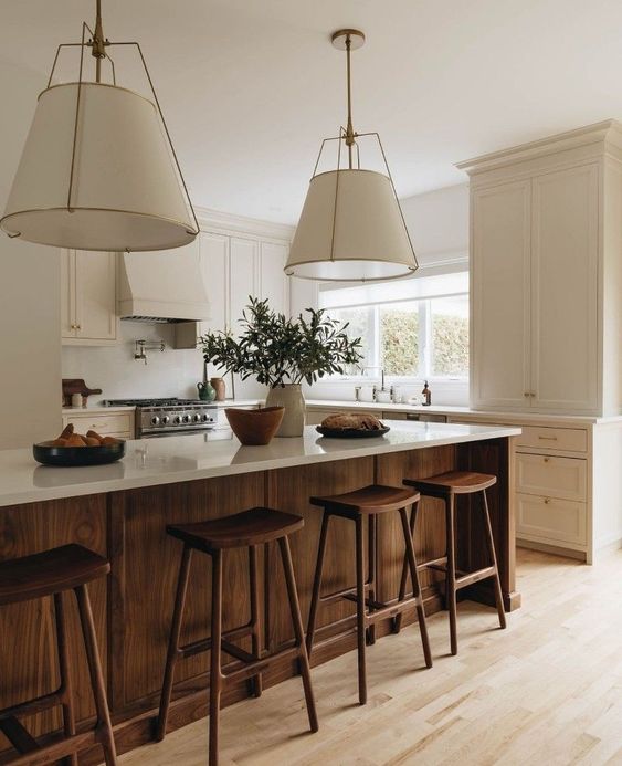a lovely modern earthy kitchen with creamy shaker cabinets, a dark-stained kitchen island, wooden stools and pendant lamps