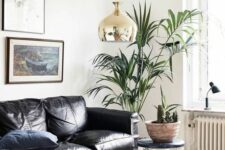 a lovely modern living room with a black leather couch, a boho printed rug, a stool, a potted plant, a copper pendant lamp and book stacks