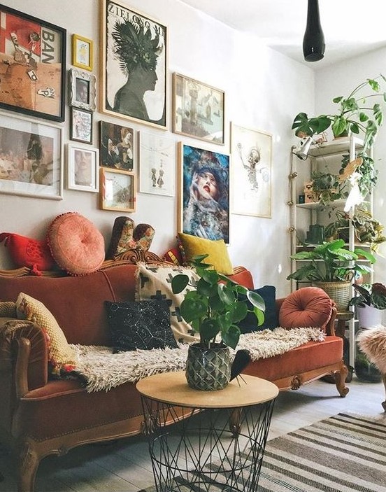a maximalist living room with a colorful gallery wlal, a rust-colored velvet vintage sofa, a round table and potted plants
