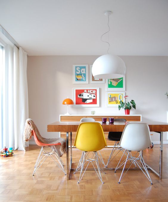 a mid-century modern dining room with a stained credenza, a stained table and colorful Eames chairs, a bright gallery wall and a white pendant lamp