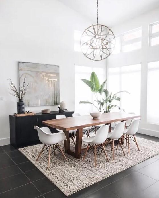 a mid-century modern dining space with a stained table and white Eames chairs, a printed rug, a black credenza, a sphere chandelier and potted plants