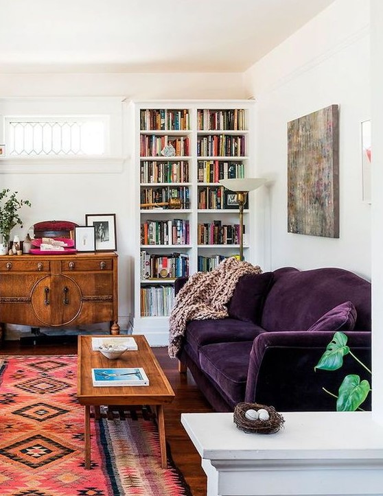 a mid-century modern living room done in neutrals and filled with color - a printed rug, a deep purple sofa, stained furniture and a built-in bookcase
