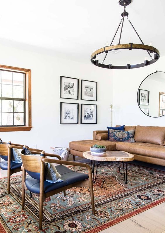 a mid-century modern living room with a brown leather sectional, a round coffee table, black chairs, a boho printed rug