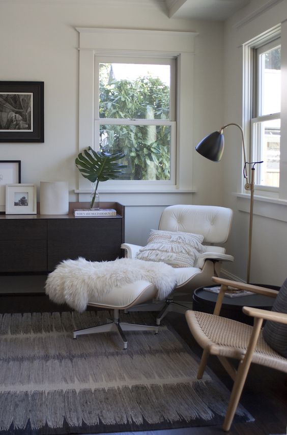 a mid-century modern living room with a dark-stained credenza, a white Eames lounger and ottoman, a rattan chair, a black side table
