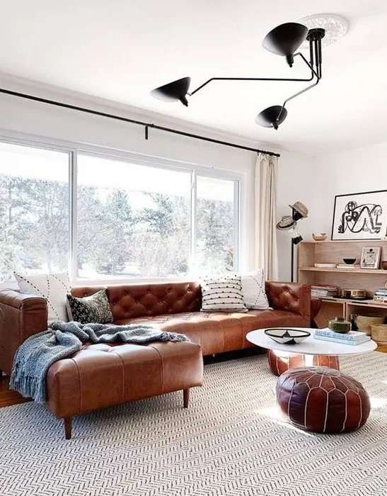 a mid-century modern neutral living room with a brown leather corner sofa and matching Moroccan poufs
