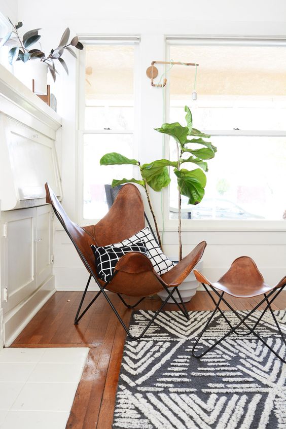 a mid-century modern nook with a brown leather butterfly and a footrest, potted plants, a printed rug and some brass touches