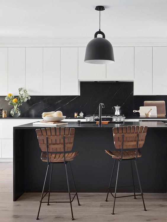 a minimalist black and white kitchen with sleek flat panel cabinets and a black kitchen island, black soapstone countertops and a backsplash, black pendant lamps
