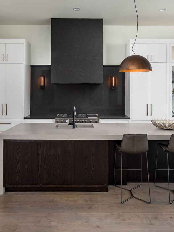 a minimalist kitchen with white cabinets and a dark-stained kitchen island, black soapstone countertops and a backsplash and a concrete countertop