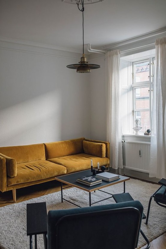 a minimalist living room with a mustard sofa, teal chairs, a low coffee table and a retro pendant lamp for a twist