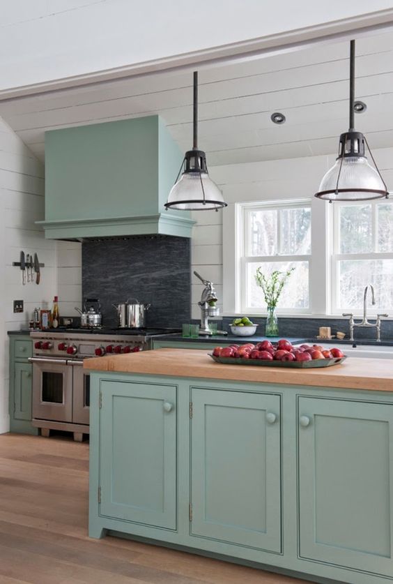 a mint blue kitchen with shaker style cabinets, black soapstone countertops and a backsplash, a butcherblock countertop and cool pendant lamps