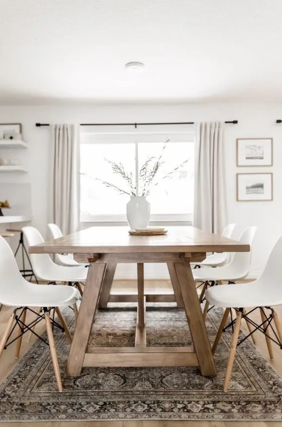a modern Scandi dining room with a stained trestle dining table, white Eames chairs, a printed rug, a vase with greenery