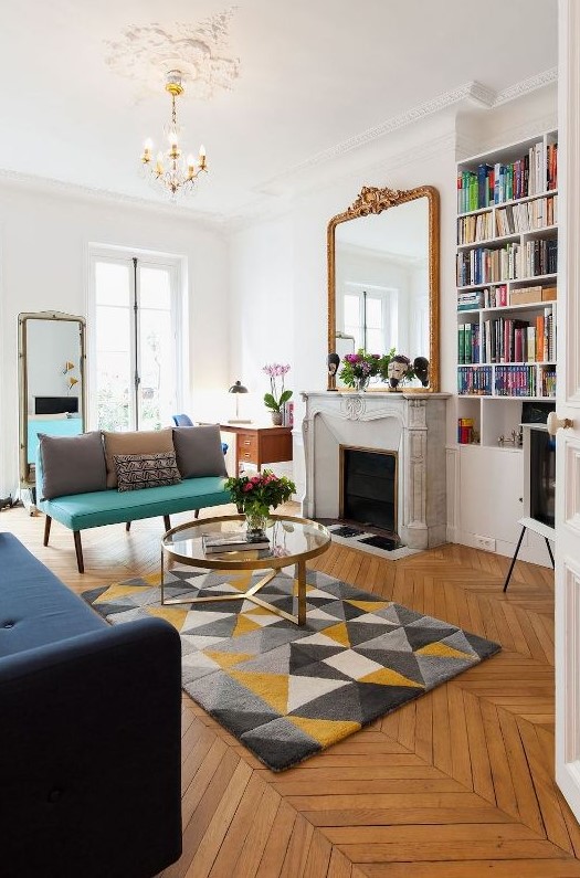 a modern and chic French living room with a French marble fireplace, a bold turquoise loveseat and a navy sofa, mirrors and a glass coffee table