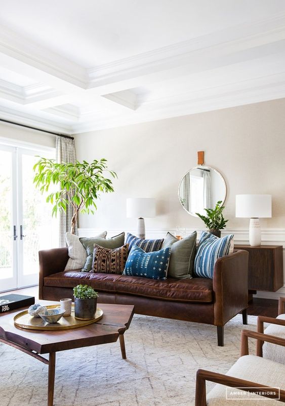 a modern boho living room with all light everything, a rich brown leather sofa, a living edge coffee table and greenery