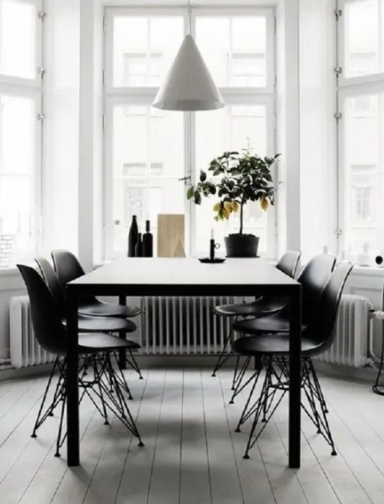 a modern dining space by the window, with a black table, black Eames chairs and a white cone pendant lamp plus a lemon tree