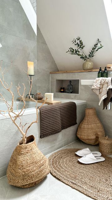 a modern earthy bathroom with grey stone-inspired tiles, a built-in tub, a floating sink, a woven rug and baskets
