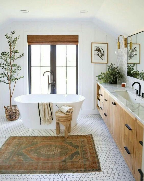 a modern earthy bathroom with hex tiles, an oval tub, a printed rug, a large vanity, black fixtures and potted plants