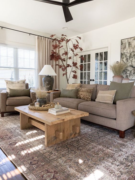 a modern earthy living room with grey seating furniture, a low wooden table, a printed rug, earthy pillows and potted plants