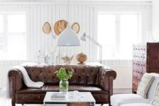 a modern farmhouse living room with white beadboard walls, vintage furniture and a brown leather Chesterfield