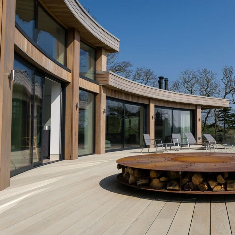 a modern outdoor space with limed oak millboard decking, grey chairs, a firepit with firewood