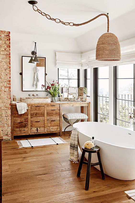 a modern rustic bathroom with a brick wall, a rough wood vanity, an oval tub, a couple of stools and a woven pendant lamp