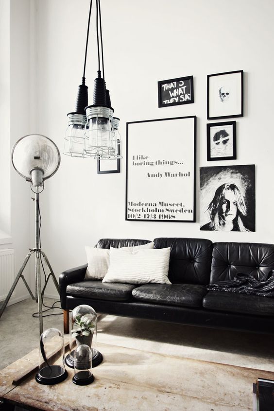 a monochromatic Scandi living room with a black leather couch, a gallery wlal, pendant jar lamps and a coffee table