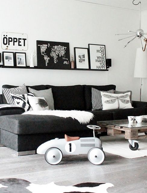 a monochromatic Scandinavian living room with a black sectional, an industrial coffee table, a black ledge with a gallery wall