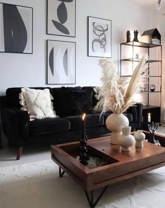 a monochromatic boho living room with a black velvet sofa, a black and white gallery wlal, a stained coffee table and a black storage unit