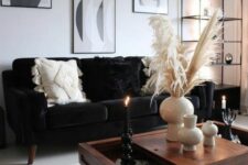 a monochromatic boho living room with a black velvet sofa, a black and white gallery wlal, a stained coffee table and a black storage unit