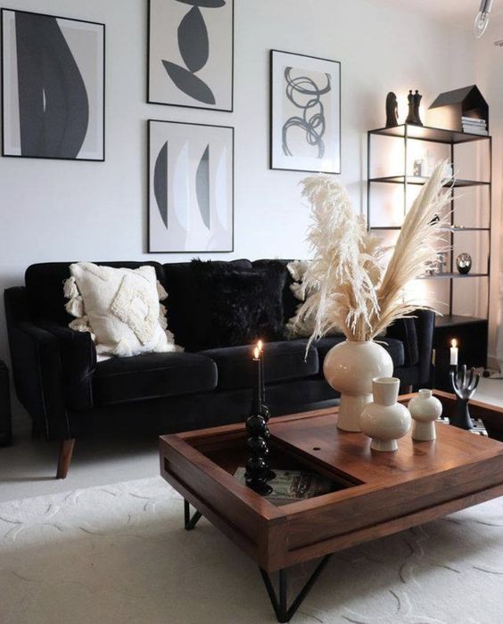 a monochromatic boho living room with a black velvet sofa, a black and white gallery wlal, a stained coffee table and a black storage unit