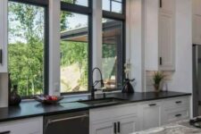 a monochromatic kitchen with shaker cabinets, black and grey stone countertops, black double-hung windows and built-in lights