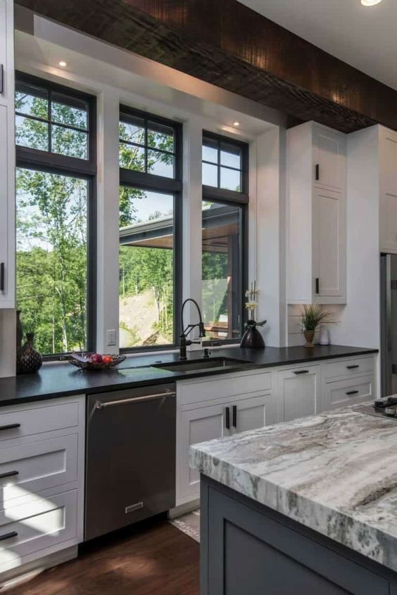 a monochromatic kitchen with shaker cabinets, black and grey stone countertops, black double hung windows and built in lights