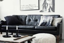a monochromatic living room with a black leather couch, a gallery wall, an industrial coffee table on casters and a white leather pouf