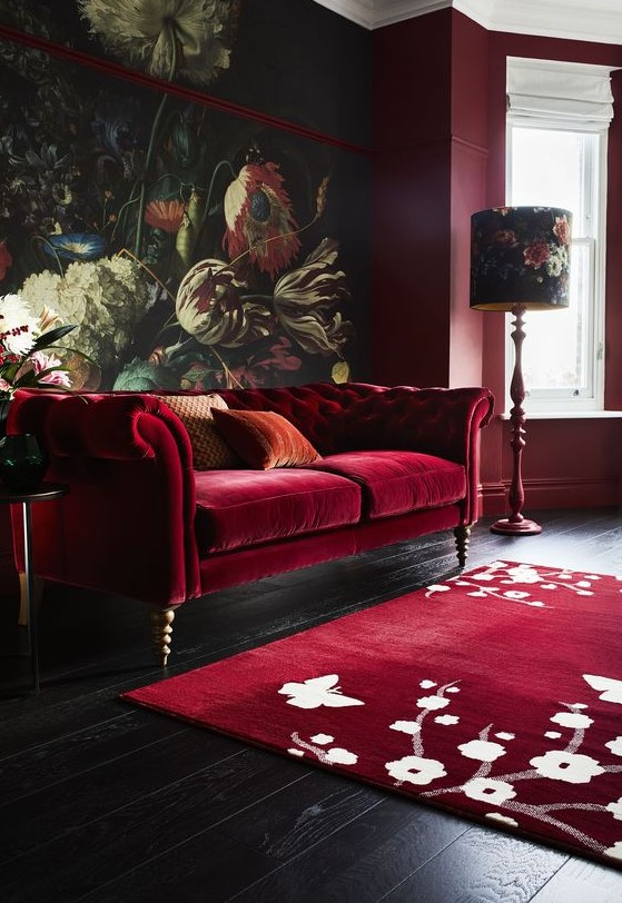 a moody and refined living room with a bold floral mural, a deep red sofa, a floral rug, floral lamps and burgundy walls