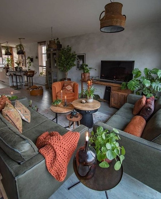 a moody grey and dark green living room with potted plants, rust pillows, a blanket and a chair and a vintage lamp